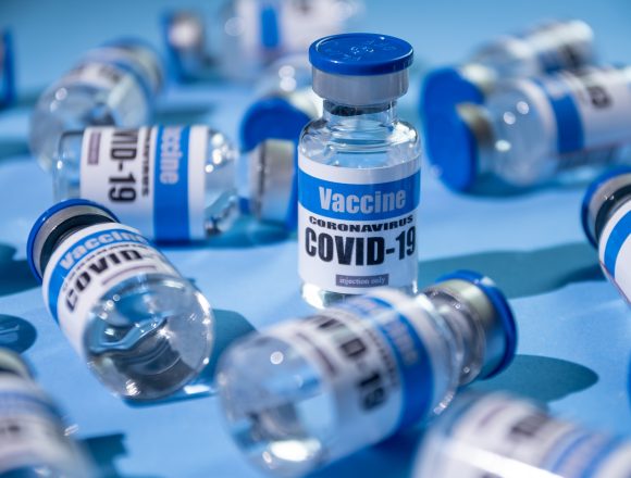Glass vials for Covid-19 vaccine on blue background. Group of Coronavirus vaccine bottles.